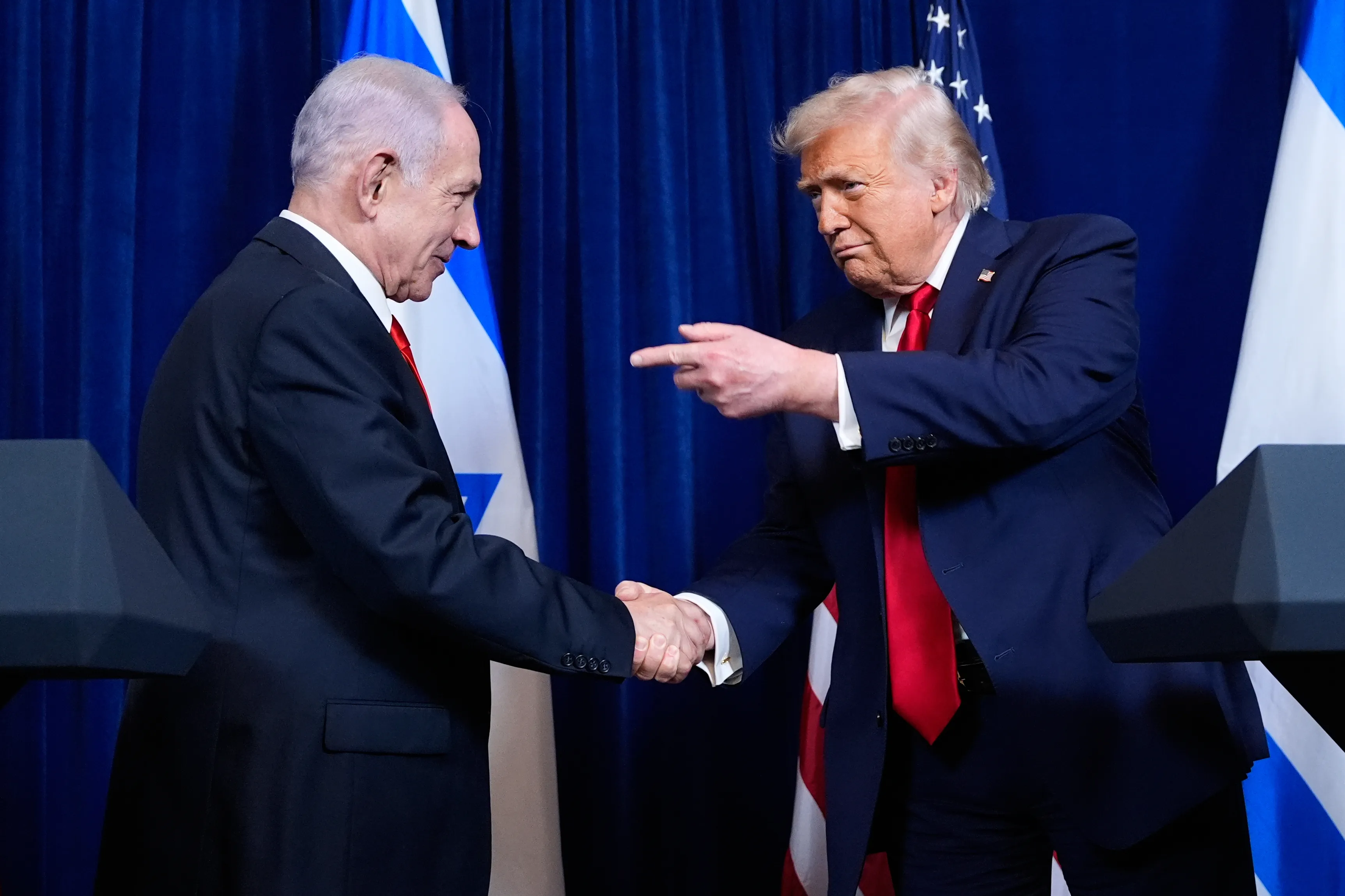 Trump points to Netanyahu as he shakes his hand.