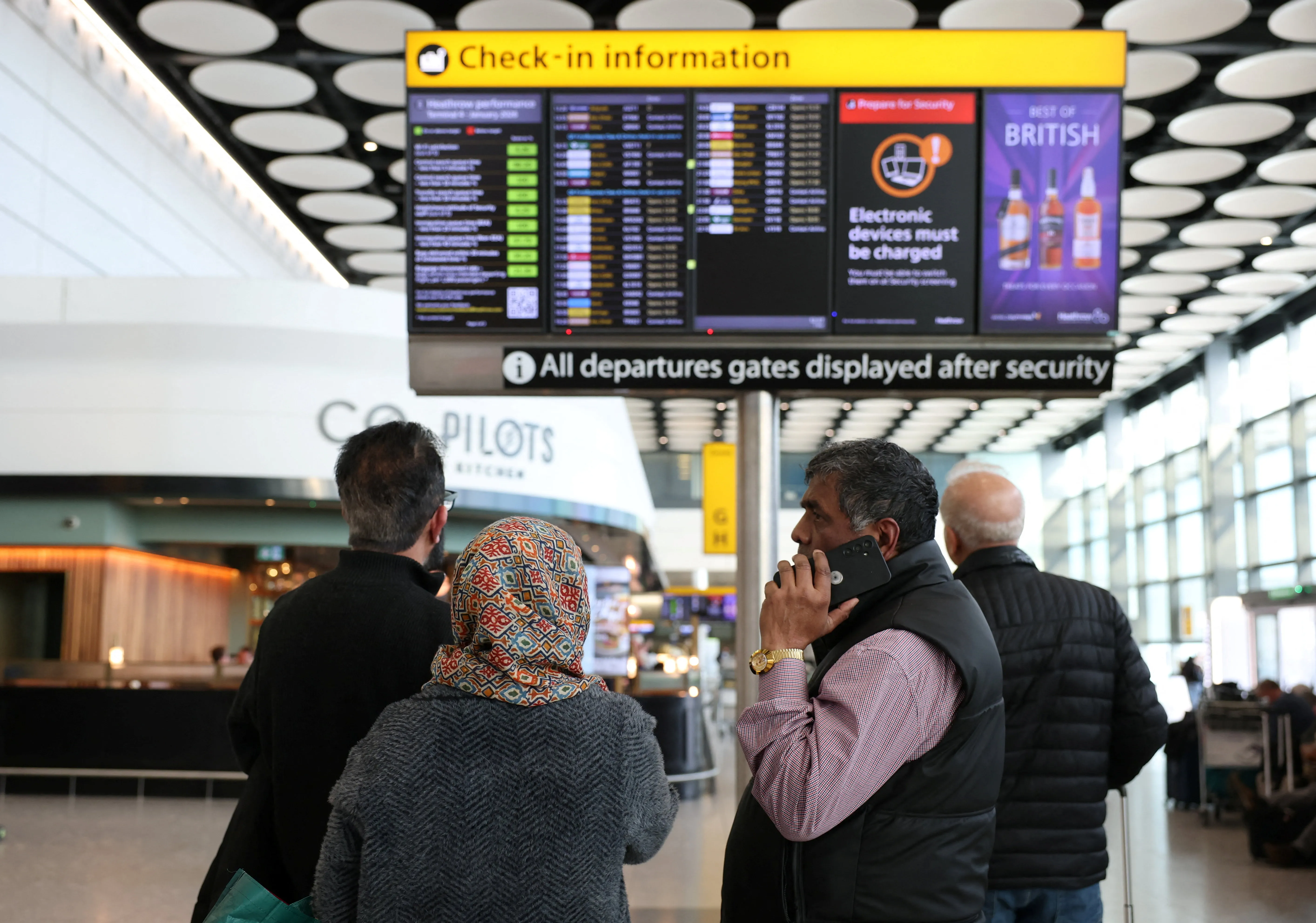Travellers check on a departure board displaying cancelled flights.