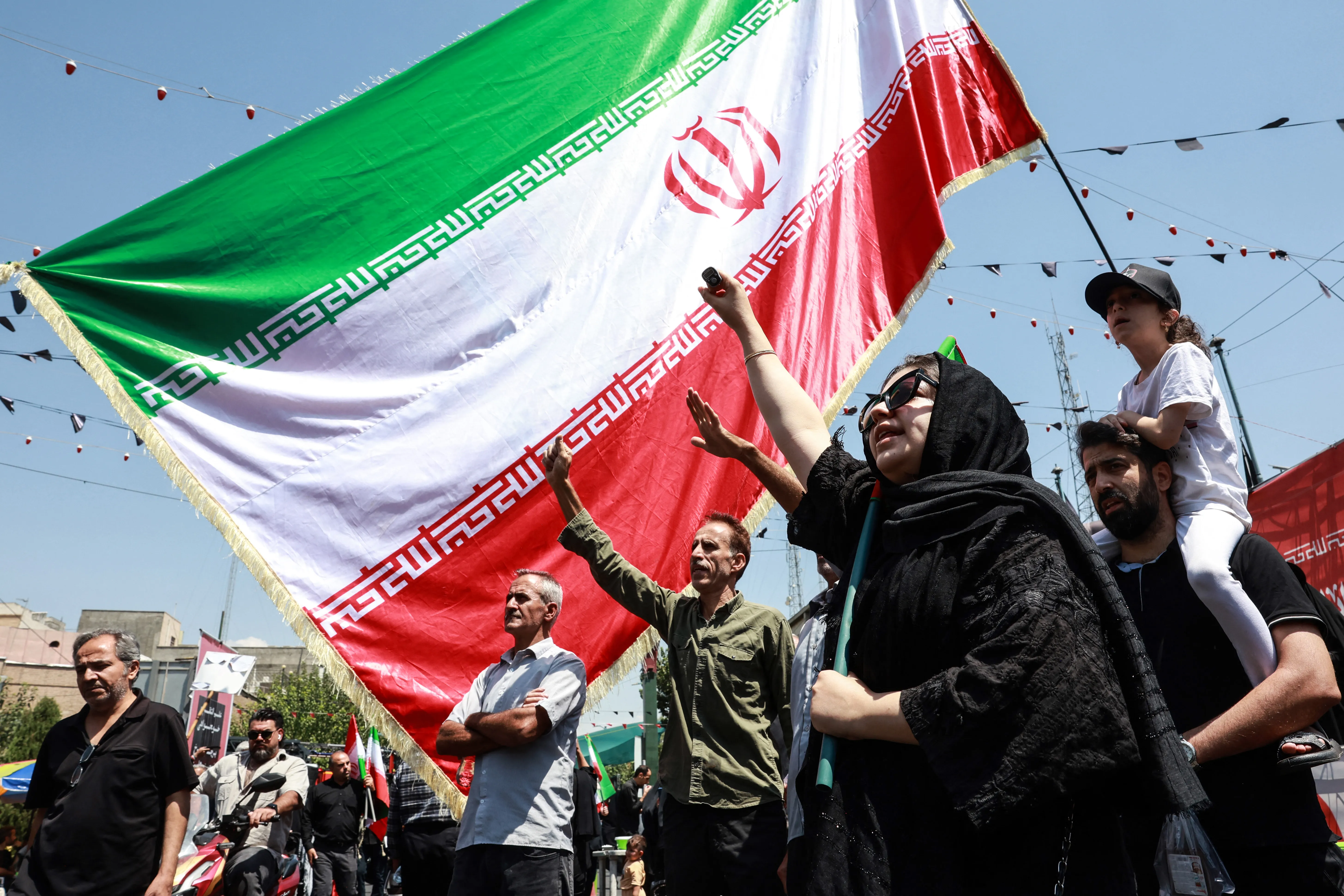 People gesture beneath an Iranian national flag as they take part in a procession.